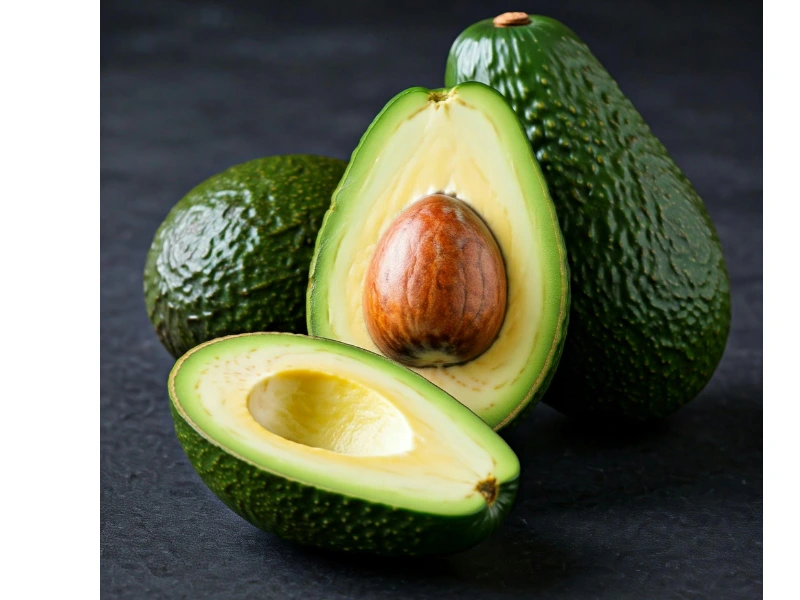 fresh whole and cut avocado showing creamy green flesh and large brown pit on dark background
