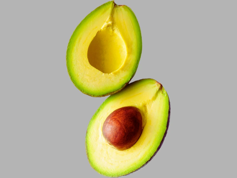 fresh avocado cut in half on a light gray background with visible green flesh and brown pit